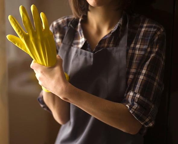 A woman holds her own hand that is inside a yellow rubber glove.